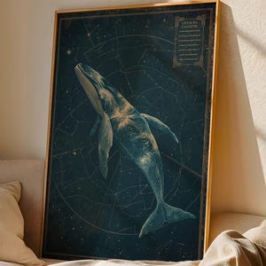 May include: A framed art print depicting a whale illustration set against a dark blue backdrop with constellations. The artwork has a vintage style, with a gold-coloured frame. The print is displayed on a beige sofa.