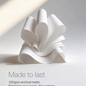 May include: A stack of white paper sheets folded into a sculptural, wavy form. The text reads: Made to last. 250gsm archival matte. Printed in your region. No customs. The paper has a smooth, matte texture and creates soft, curved shadows.