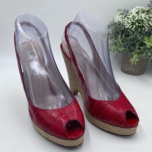 May include: A pair of red peep-toe wedge shoes featuring a textured crocodile-embossed pattern on the upper material. The shoes have a slingback strap and a tan woven jute-style platform wedge heel, providing a distinct contrast to the red leather.
