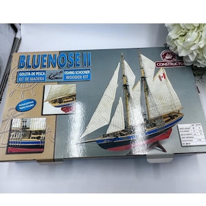 May include: A Bluenose II fishing schooner wooden model kit box featuring a large illustration of the ship with white sails, a blue hull, and a red bottom. The box includes text labels, inset photos of the model, and a technical specification chart.