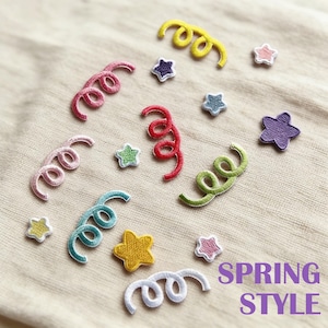 Puede incluir: Parches bordados en forma de estrellas y espirales, en tonos de amarillo, rosa, rojo, verde, azul y blanco. El texto "SPRING STYLE" se muestra en morado y blanco.