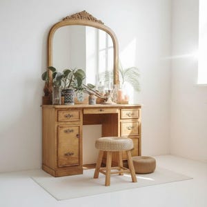 May include: A vintage wooden vanity with a large arched mirror, drawers, and a small stool. The vanity is made of light-colored wood and is decorated with plants and candles. The stool is made of woven material and wood.
