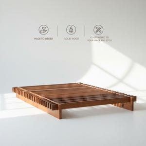 Peut inclure: Un cadre de lit en bois avec un design à lattes. Le cadre est en bois massif et est de couleur marron chaud. Le cadre de lit est présenté sur un fond blanc. Le texte de l'image indique "MADE TO ORDER", "SOLID WOOD" et "CUSTOMIZED TO YOUR SPACE AND STYLE".