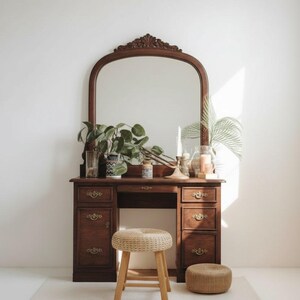 May include: A vintage wooden vanity with a large arched mirror, drawers, and decorative hardware. The vanity is adorned with plants, candles, and a woven stool. The overall aesthetic is warm and inviting, perfect for a bedroom or dressing area.