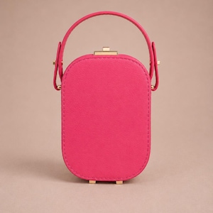 May include: A bright pink, oval-shaped handbag with a textured surface, featuring a single top handle attached with gold-toned metal hardware. The bag has a secure gold-toned clasp closure at the top and small gold-toned feet at the base.