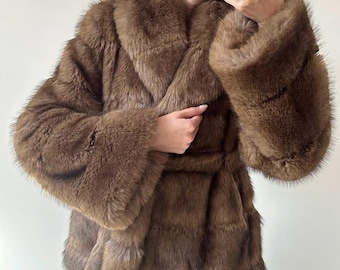 May include: A brown faux fur coat with a wide collar and flared sleeves. The coat has a belt that cinches at the waist. The fur appears soft and plush, with a rich, warm color. The coat is a medium length.