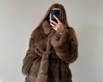 May include: A brown faux fur coat with a tie closure. The coat has a plush texture and a classic design. The sleeves are long, and the coat appears to be knee-length. The coat is a warm, stylish outerwear option.