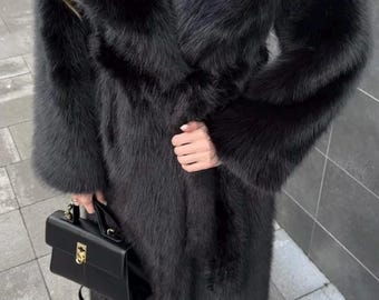 May include: A long, black faux fur coat with a wide collar and a matching belt. The coat is paired with a black handbag and gold-tipped shoes. The coat's texture is soft and luxurious, perfect for cold weather.
