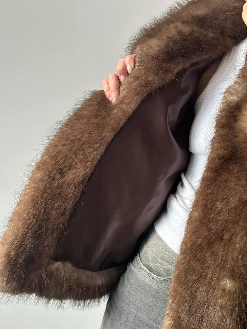 May include: A brown faux fur coat with a dark brown satin lining. The coat has a plush, textured appearance and is open, revealing the interior lining. The fur is a rich, warm brown color.
