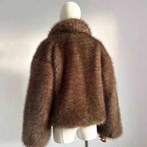 May include: A brown faux fur jacket with a wide collar and long sleeves. The jacket is displayed on a mannequin against a plain white background. The fur appears soft and plush.