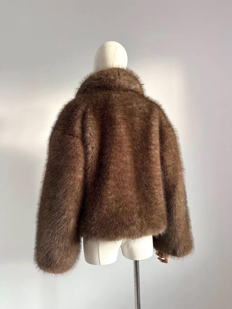 May include: A brown faux fur jacket with a wide collar and long sleeves. The jacket is displayed on a mannequin against a plain white background. The fur appears soft and plush.