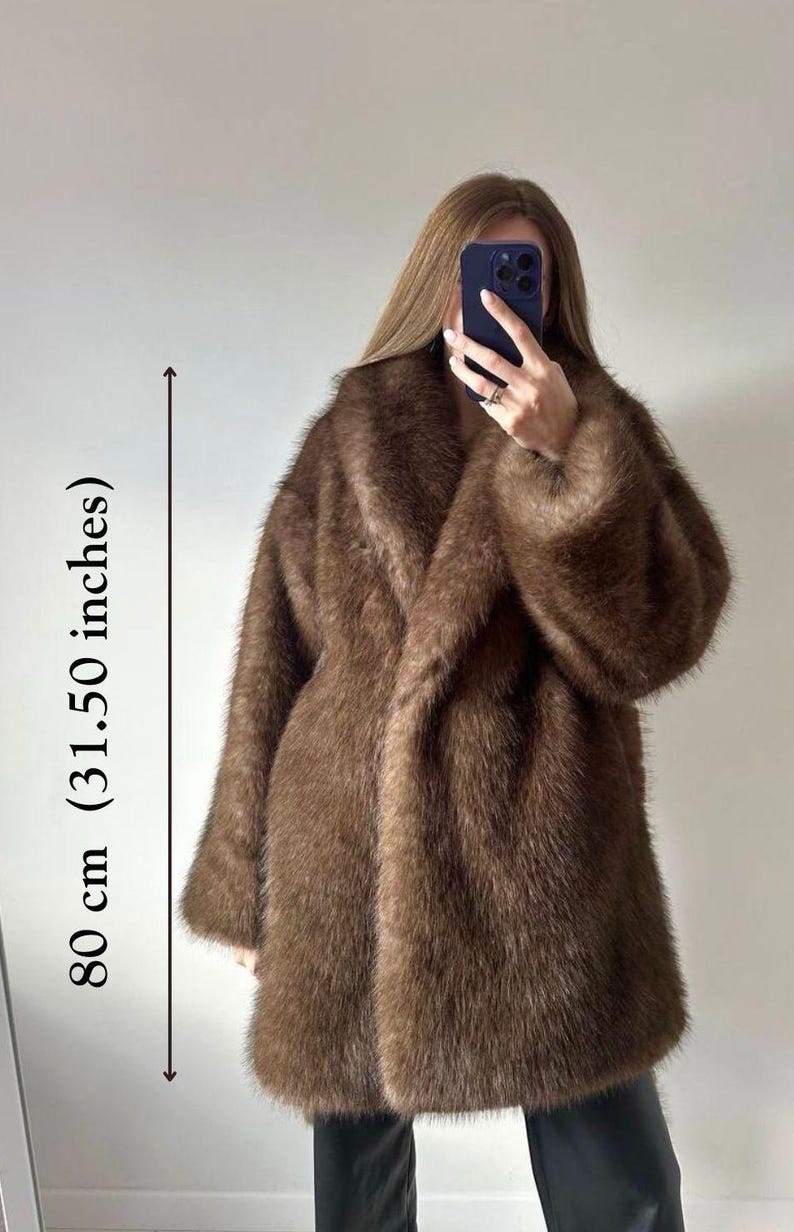 May include: A brown faux fur coat, approximately 31.50 inches in length, with a wide collar and long sleeves. The coat has a soft, textured appearance and is worn open. The overall style is a classic, oversized design.
