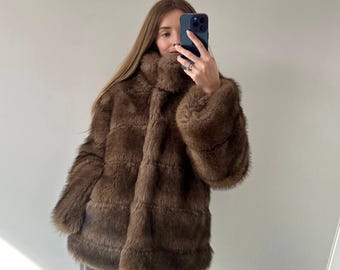 May include: A brown faux fur coat with a high collar and long sleeves. The coat has a textured appearance and a slightly oversized fit. The color is a rich, warm brown, suitable for colder weather. The coat is a stylish outerwear option.