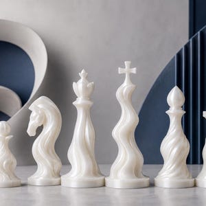 Könnte beinhalten: Ein Set aus sechs weißen Schachfiguren mit einem markanten, wirbelnden und fließenden Design. Die Sammlung umfasst einen Bauern, Springer, eine Dame, einen König mit Kreuz, einen Läufer und einen Turm, alle mit glatter Perlmuttoptik.