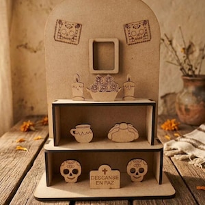 Può includere: Un espositore a più livelli in legno marrone chiaro con decorazioni tagliate al laser, tra cui due teschi di zucchero, una piccola cornice, candele, fiori, una tazza, pane e una lapide con l'incisione "DESCANSE EN PAZ" alla base.