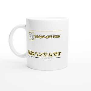 以下が含まれることがあります： 白いセラミック製のマグカップ。Aの文字と日本語の文字が書かれた2枚の重なった書類の黄色いアイコンが描かれています。アイコンの下には、黒い文字に黄色の縁取りで「TRANSLATE THIS:」と「私はハンサムです」というテキストが印刷されています。