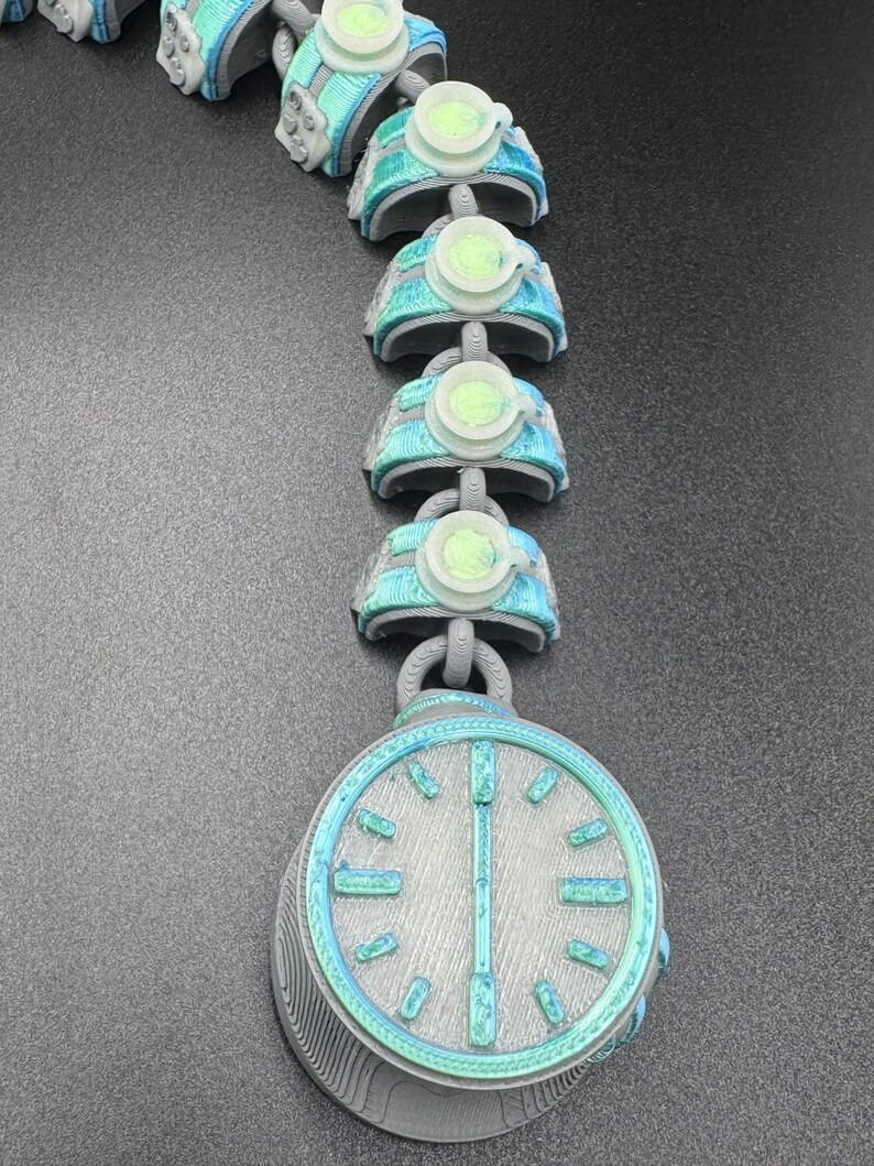 May include: A futuristic necklace with a large, round pendant resembling a pocket watch. The necklace is grey with teal and light green accents. The chain links have a similar design, creating a cohesive, sci-fi aesthetic.