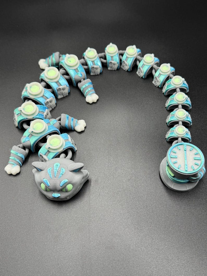 May include: A 3D-printed articulated cat toy in grey, blue, and green. The toy features a cat head, segmented body, and a clock-like tail end. The body segments have circular details and the cat's eyes glow green.