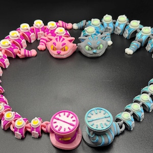 May include: A collection of articulated cat figures and clock-shaped objects in pink, blue, and grey, with yellow and white details. The arrangement is set against a dark background. The figures are arranged in a circular pattern.