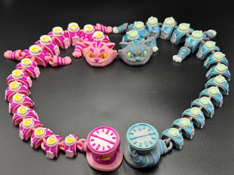 May include: A collection of articulated cat figures and clock-shaped objects in pink, blue, and grey, with yellow and white details. The arrangement is set against a dark background. The figures are arranged in a circular pattern.