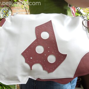 May include: A white leather handbag with a red leather cutout of a cheese shape. The bag has a white stitch around the edges and a metal chain strap.