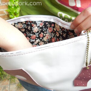 May include: White leather purse with a pink accent and a floral print lining. The purse has a zipper closure and a gold chain strap.