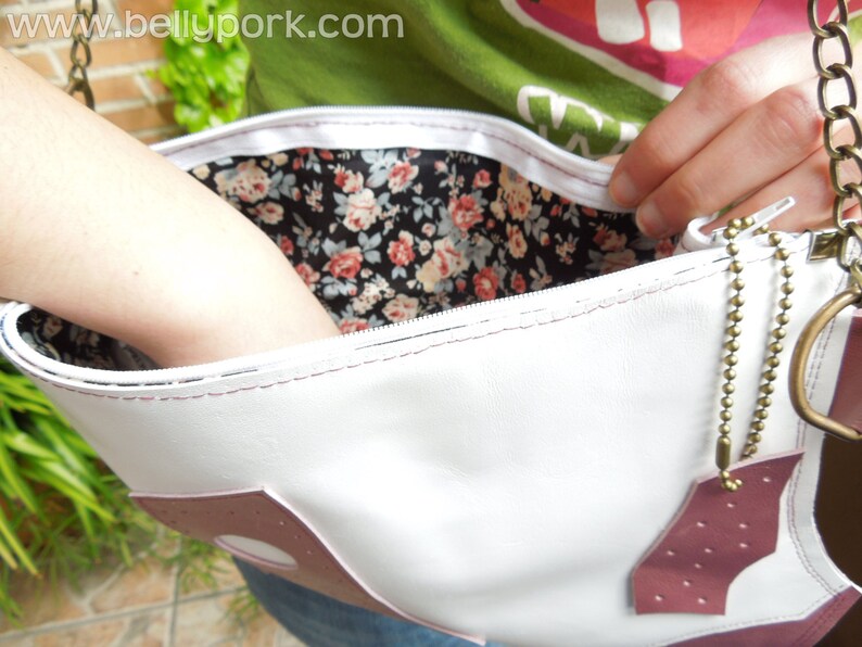 May include: White leather purse with a pink accent and a floral print lining. The purse has a zipper closure and a gold chain strap.