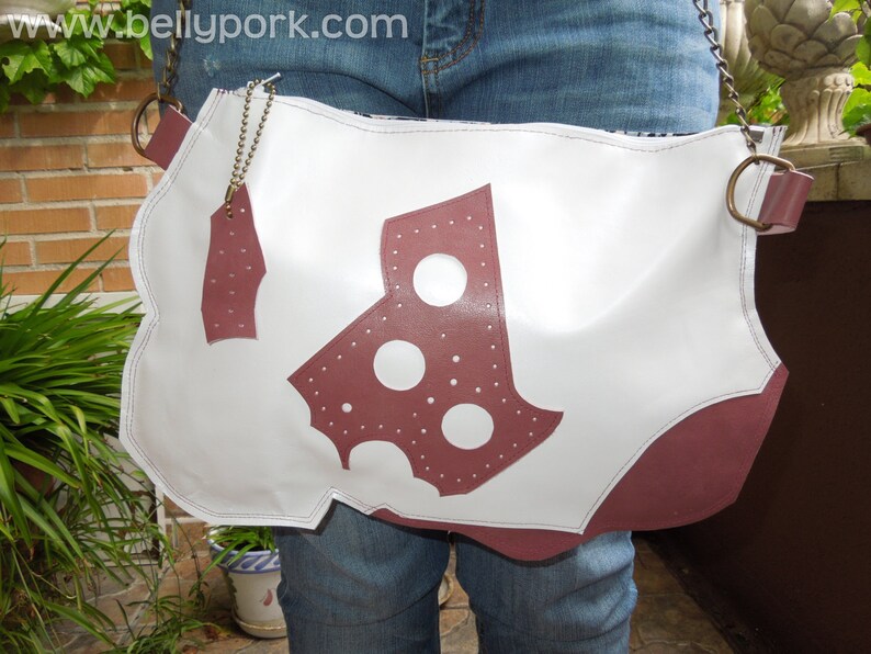May include: A white leather bag with a burgundy leather design. The bag has a strap and a metal buckle. The bag is worn over the shoulder.