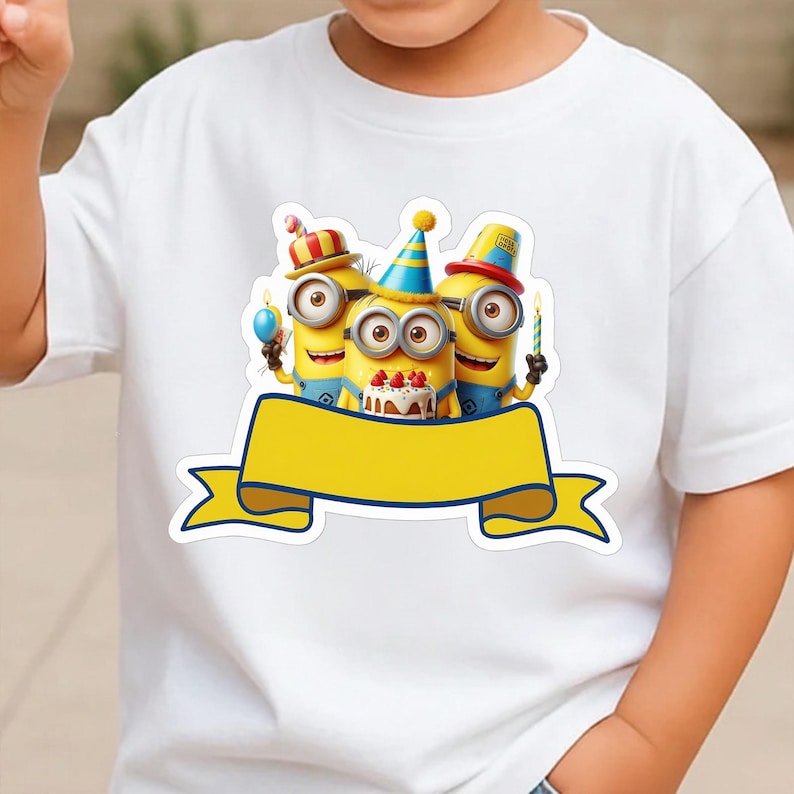 K&ouml;nnte beinhalten: Ein wei&szlig;es Kurzarm-T-Shirt mit einer Grafik von drei gelben Minion-Figuren, die bunte Partyh&uuml;te tragen und eine Geburtstagstorte mit Kerzen halten, platziert &uuml;ber einem gro&szlig;en, leeren gelben Banner mit dunkelblauem Rand.