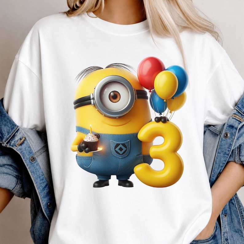 K&ouml;nnte beinhalten: Ein wei&szlig;es T-Shirt mit einer Grafik eines gelben, ein&auml;ugigen Minion-Charakters in blauer Latzhose. Die Figur h&auml;lt einen kleinen Cupcake mit einer brennenden Kerze und steht neben einem gro&szlig;en gelben Luftballon in Form einer Drei sowie einer Ansammlung roter, gelber und blauer Luftballons.