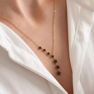May include: A gold-tone chain necklace featuring a Y-shaped drop design adorned with five small, black, star-shaped charms. Each star is encrusted with tiny black stones, creating a delicate and symmetrical arrangement that hangs from the center.