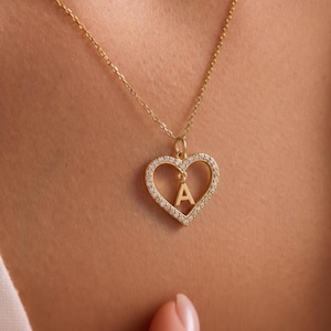Op de afbeelding: Een goudkleurige ketting met een hartvormige hanger. De hanger is bezet met kleine, heldere steentjes en heeft de letter "A" in het midden. De ketting heeft een fijne schakel.