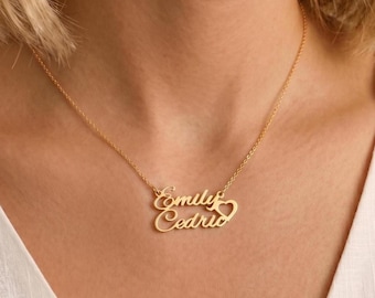 May include: A gold-toned metal necklace featuring a delicate chain and a custom nameplate pendant. The pendant displays the names Emily and Cedric in a cursive script font, with a small heart shape integrated into the design on the right side.