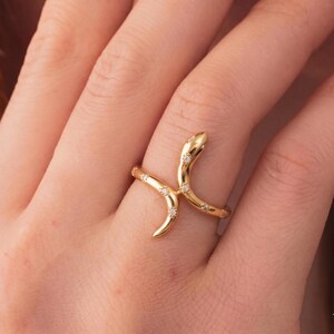 Peut inclure: Une bague serpent dorée ornée de petits pierres précieuses transparentes. La bague est enroulée autour d'un doigt, avec la tête et la queue du serpent courbées vers le haut. Un bijou unique.