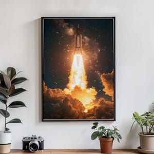 May include: A framed print depicts a rocket launching into space. The rocket is white and orange, with a bright orange flame and smoke billowing from the base. The background is a dark night sky filled with stars and clouds.