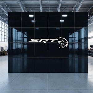 Può includere: Un muro nero con il logo SRT bianco e un emblema Hellcat stilizzato. Il muro è diviso in pannelli quadrati e riflette l'ambiente circostante. Il logo è centrato sul muro.
