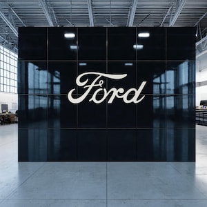May include: A large black wall with the white Ford logo. The wall is made of square tiles and reflects the surrounding environment. The logo is in a cursive font.