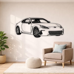 Op de afbeelding: Een wit metalen wandkunstwerk dat een sportwagen afbeeldt. De auto is een coupé met zwarte wielen en een gedetailleerde grille. Het kunstwerk is bevestigd aan een witte muur, boven een beige fauteuil en een ronde poef.