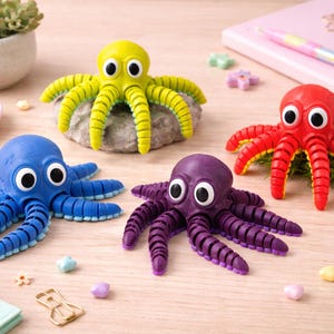 Op de afbeelding: Vier kleurrijke octopusbeeldjes in geel, blauw, rood en paars met grote witte ogen. Het octopus speelgoed staat op een licht houten oppervlak met kleine decoratieve items op de achtergrond.
