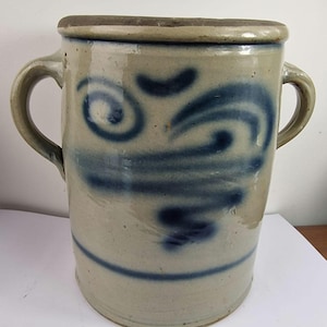 Könnte beinhalten: Ein Steingutkrug mit zwei Griffen und einem dunklen Rand. Der cremefarbene Körper ist mit blauen Wirbel- und Linienmustern verziert. Der zylindrische Behälter ist ein Vintage-Stück.