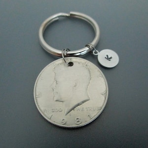 May include: Silver keychain with a 1968 half dollar coin and a small charm with the letter "K" on it.