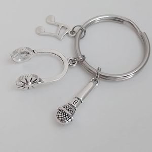 May include: Silver-toned keychain featuring musical symbols. Includes a treble clef, headphones, and a microphone charm. The keychain is attached to a large, round key ring. Ideal for music lovers.