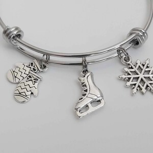 May include: A silver bangle bracelet with three charms: a snowflake, a pair of mittens, and an ice skate.