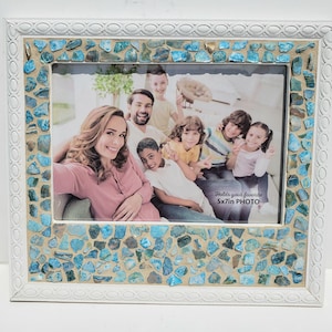 May include: White picture frame with a mosaic of blue and white tiles surrounding the opening. The frame holds a 5x7 inch photo of a family.