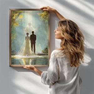 May include: A framed painting depicts a wedding scene with a bride in a white gown and a groom in a suit, standing before a figure in a bright light. The artwork has a soft, ethereal quality, with a wooden frame.