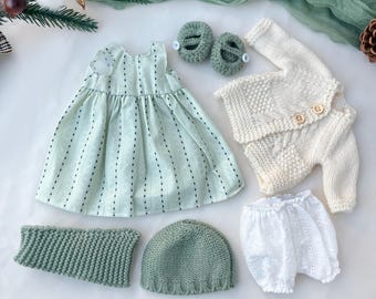 Peut inclure: Un ensemble de vêtements pour bébé comprenant une robe vert clair à rayures noires, un cardigan et un pantalon en tricot crème, un bonnet en tricot vert, un chauffe-cou en tricot vert, un bloomer blanc et des chaussures en tricot vert.