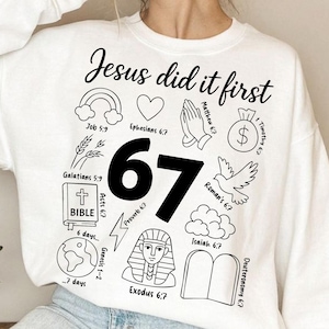 以下が含まれることがあります： 「Jesus did it first」の黒い文字がプリントされた白いスウェットシャツ。虹、ハート、祈りの手、お金の袋、鳩、雲、その他の宗教的シンボルがデザインされています。「67」の数字が大きく表示されています。