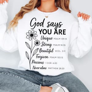May include: White sweatshirt with the text "God says YOU ARE" and a floral design. Below the text are the words "Unique, Strong, Beautiful, Forgiven, Precious, Never alone" with corresponding Bible verses.