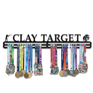 May include: Black metal medal display with the words "CLAY TARGET" and silhouettes of a shooter and a helmet. Colorful ribbons with medals hang below. A great way to display achievements.