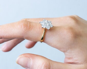Può includere: Un anello d'oro con un gruppo di pietre preziose trasparenti in un design floreale. L'anello è su un dito, mostrando gli intricati dettagli dell'incastonatura e la brillantezza delle pietre. La fascia dell'anello è dorata.